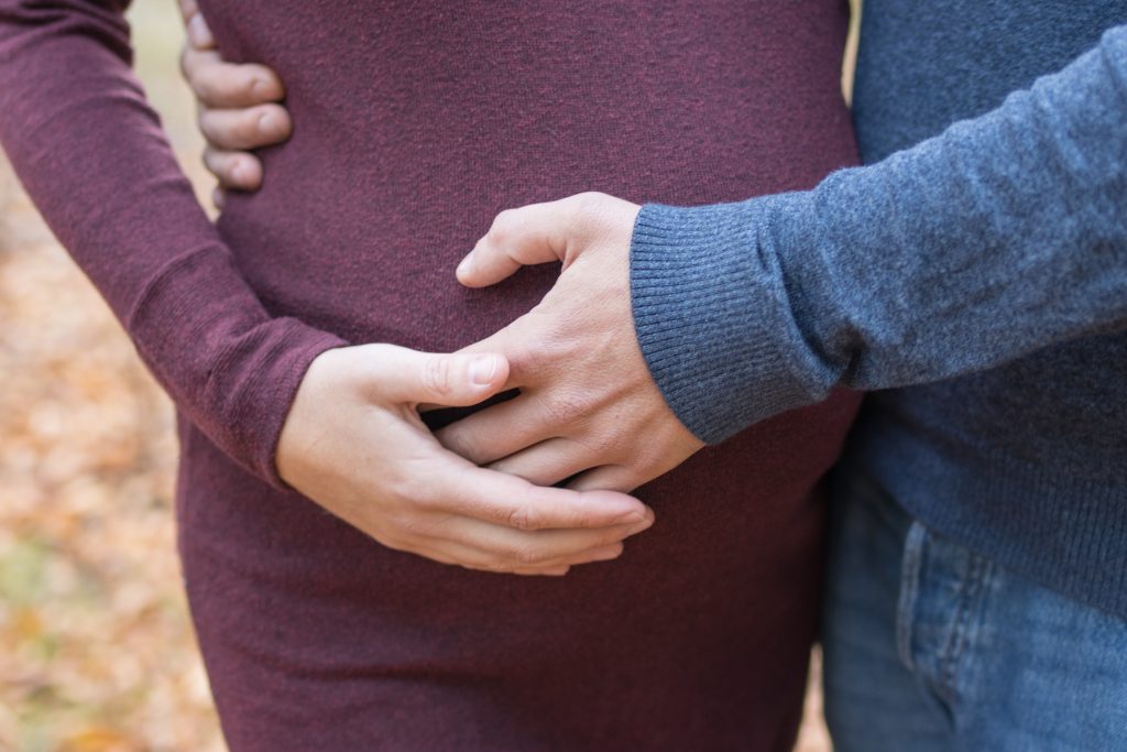 Mann streichelt seiner schwangeren Frau den BAuch, Frau mit Babybauch an der Elbe in hoher Wiese stehend mit Herbstlichem Kleid.