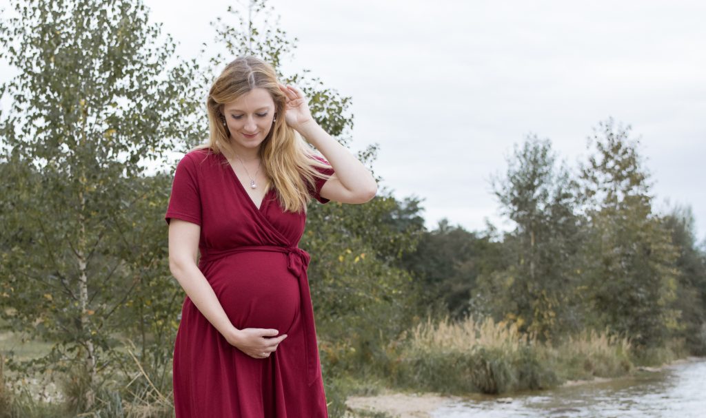 Schwangere Frau in rotem Kleid am See.