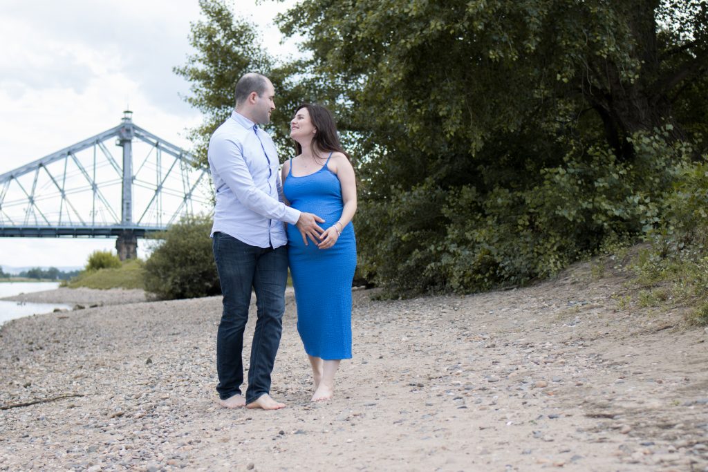 Mann streichelt seiner schwangeren Frau den BAuch, Frau mit Babybauch an der Elbe entlang laufend.